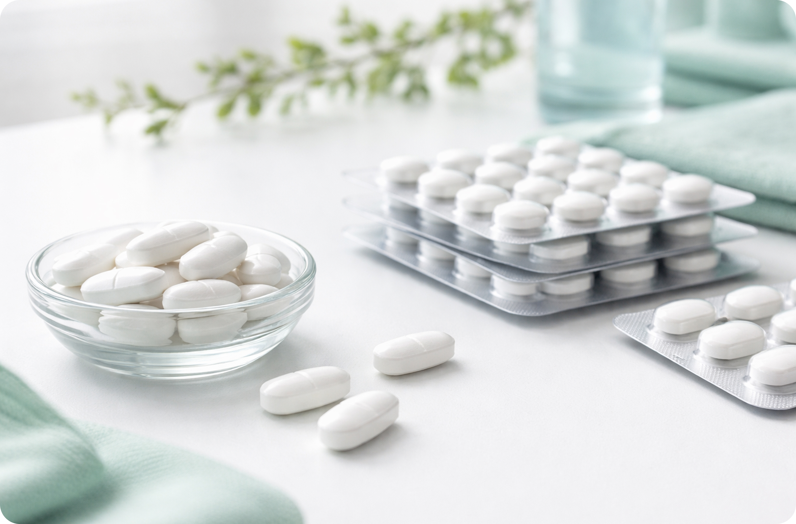 White tablets in a glass bowl with blister packs arranged on a bright table
